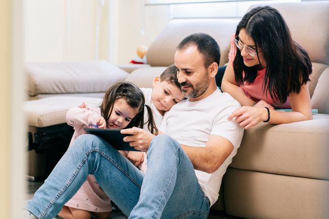 Eltern spielen mit Kindern auf der Coach am Tablet - mehr Zeit für die Familie